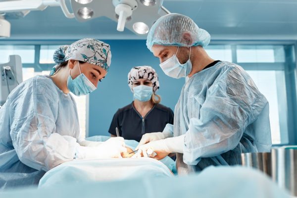 Doctors performing abdominoplasty surgery in the hospital. Focus on male plastic surgeon doing abdominal plastic surgery in operating room. Concept of tummy tuck and cosmetic surgery