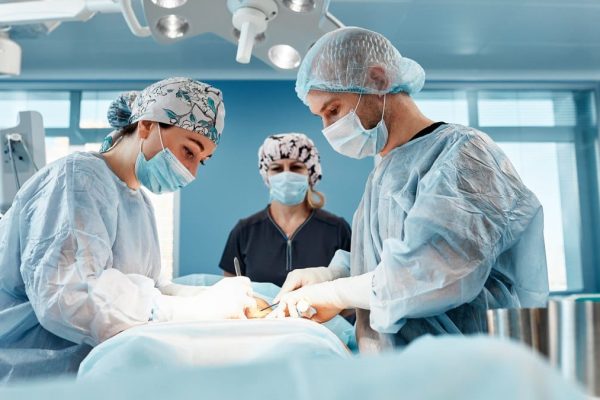 Doctors performing abdominoplasty surgery in the hospital. Focus on male plastic surgeon doing abdominal plastic surgery in operating room. Concept of tummy tuck and cosmetic surgery